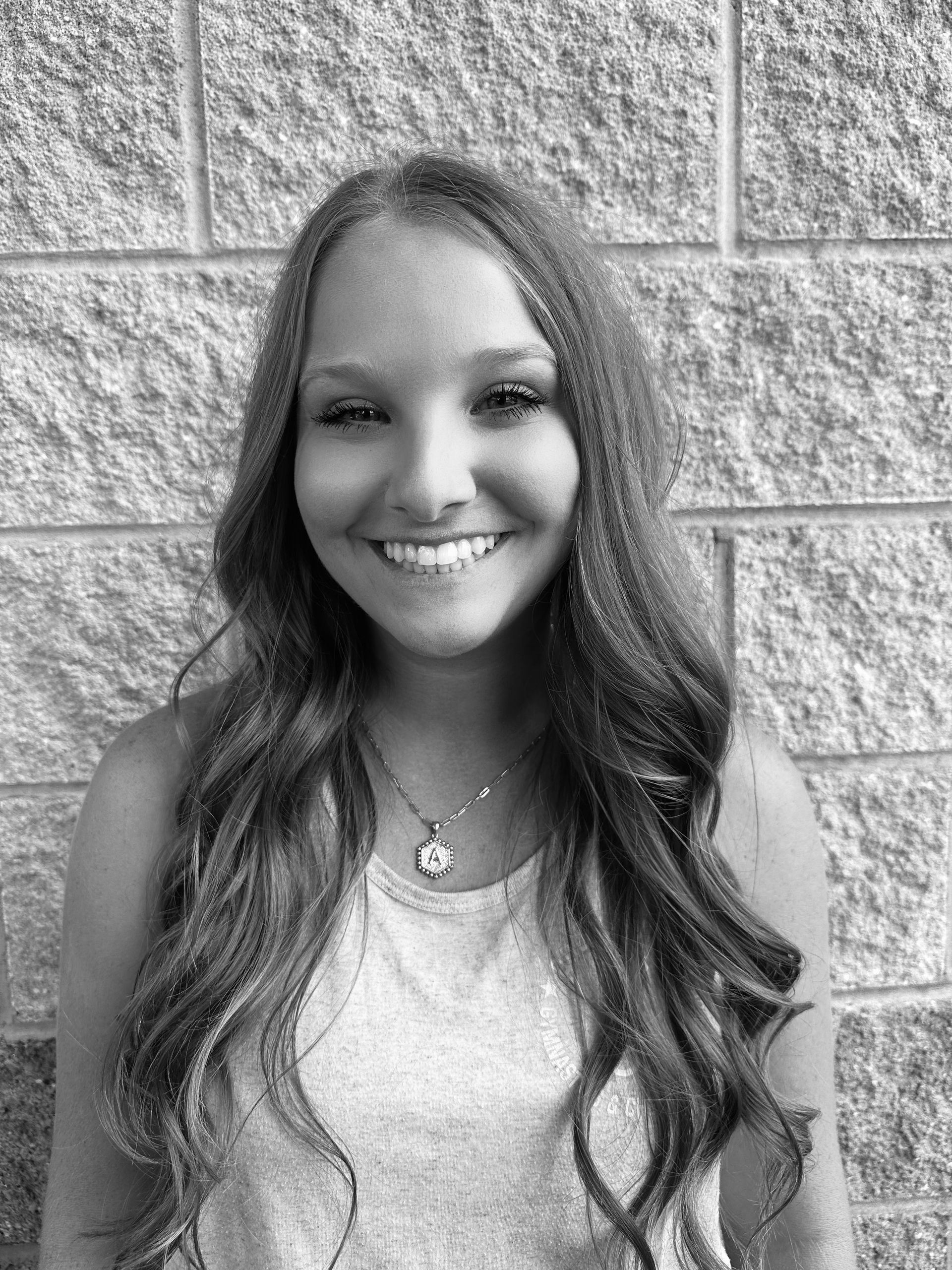 A black and white photo of a woman smiling in front of a brick wall.