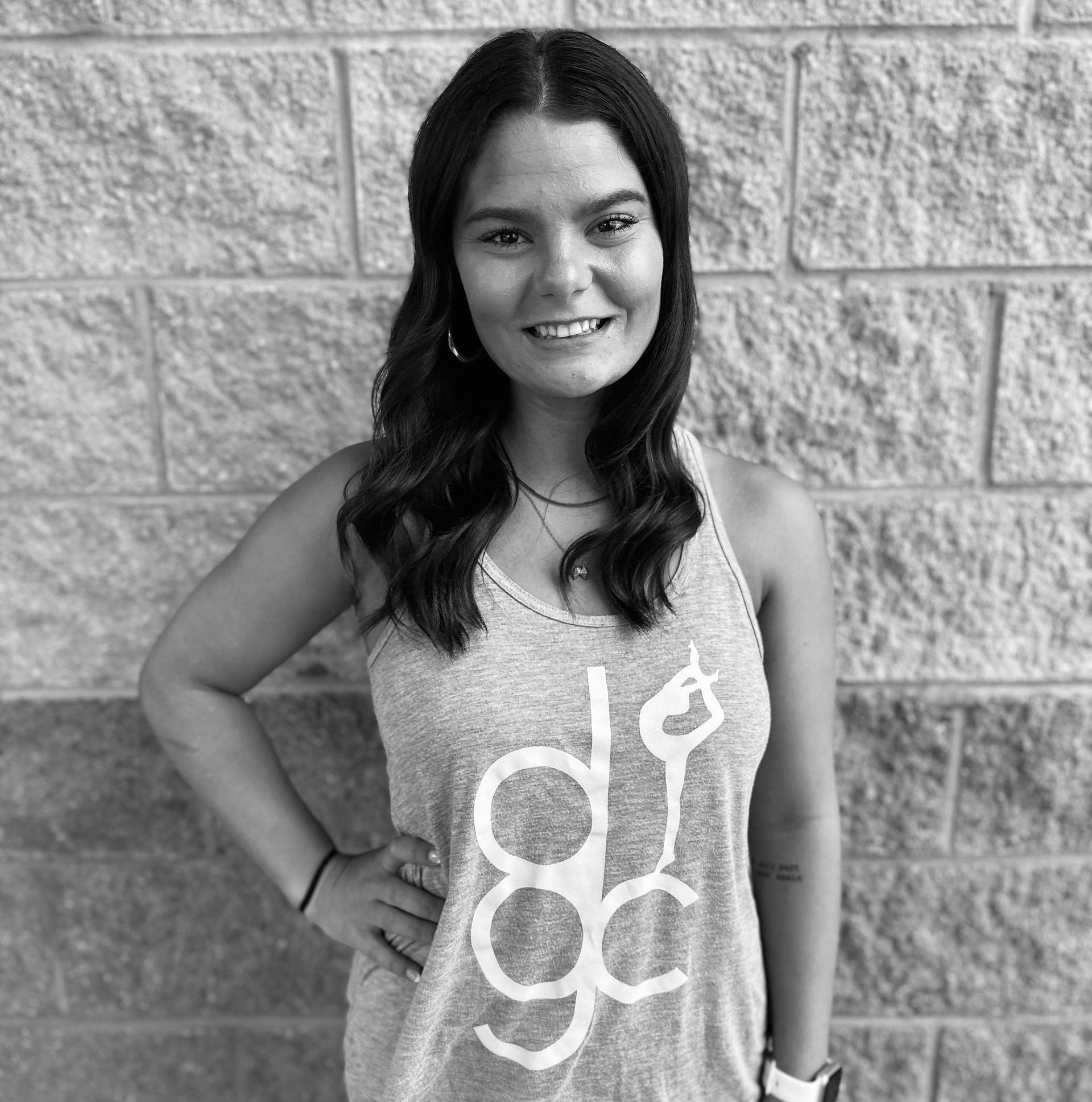 A woman in a tank top is standing in front of a brick wall.