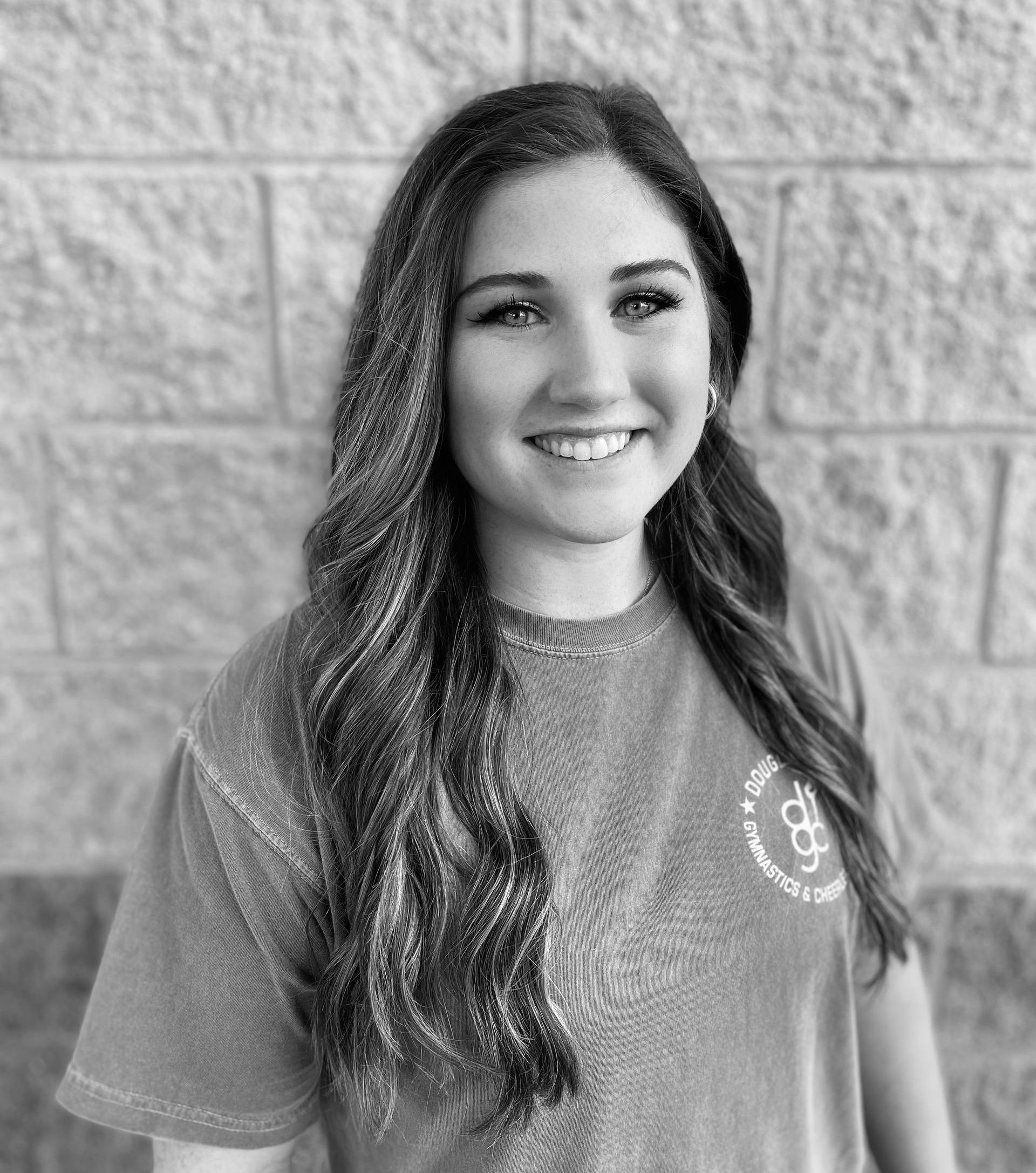 A black and white photo of a woman smiling in front of a brick wall.