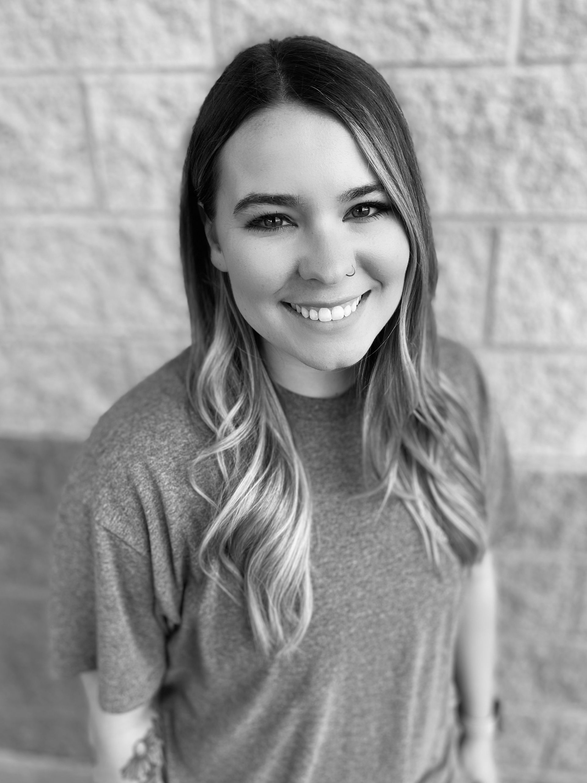 A black and white photo of a woman smiling in front of a brick wall.