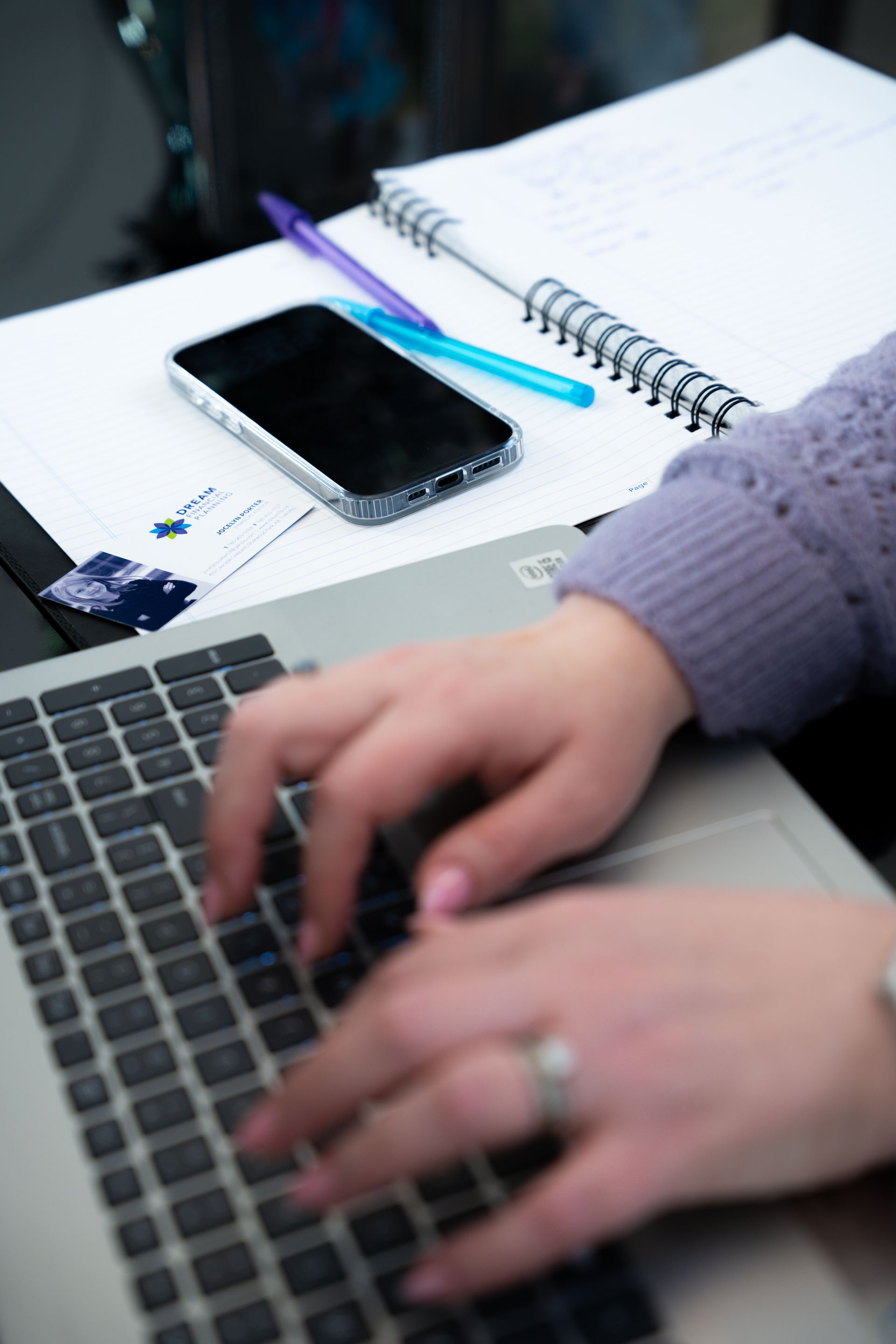 Hands stacked together on a table, signifying teamwork; papers and a laptop are visible.