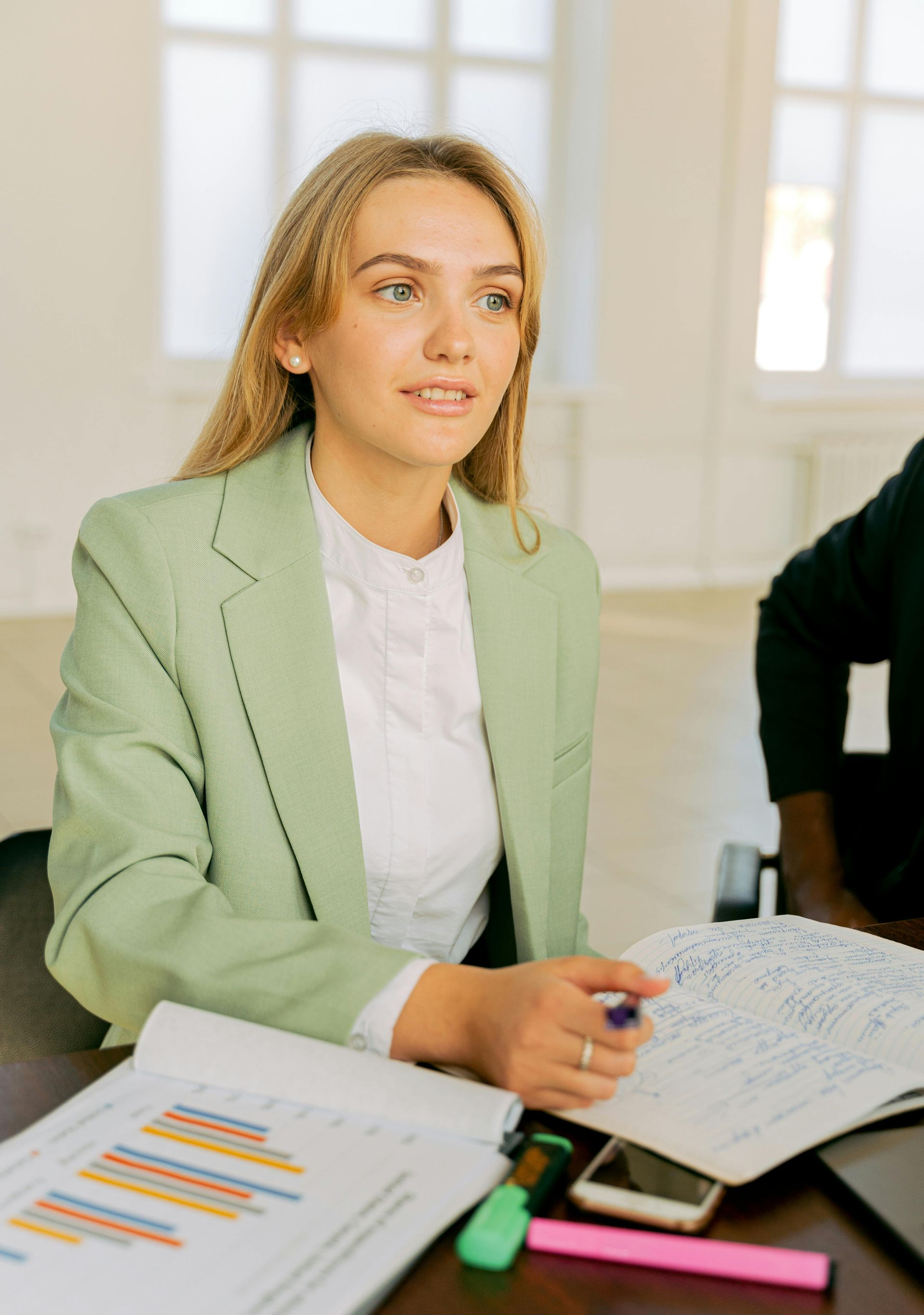 Woman in green blazer at a table with papers, notebook, and phone.
