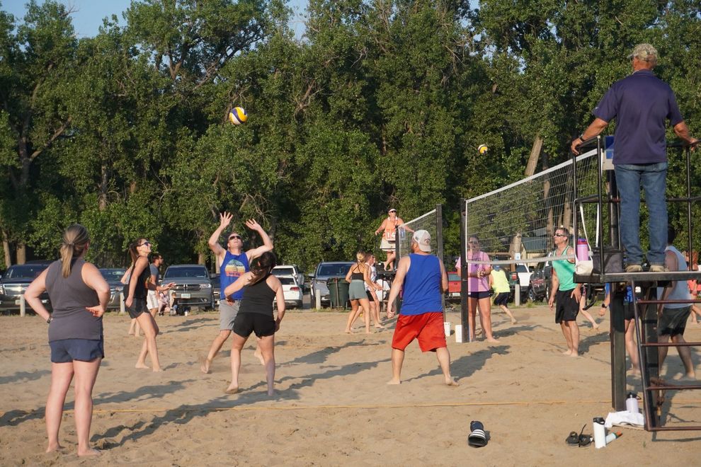 2 teams playing sand volleyball in a park.