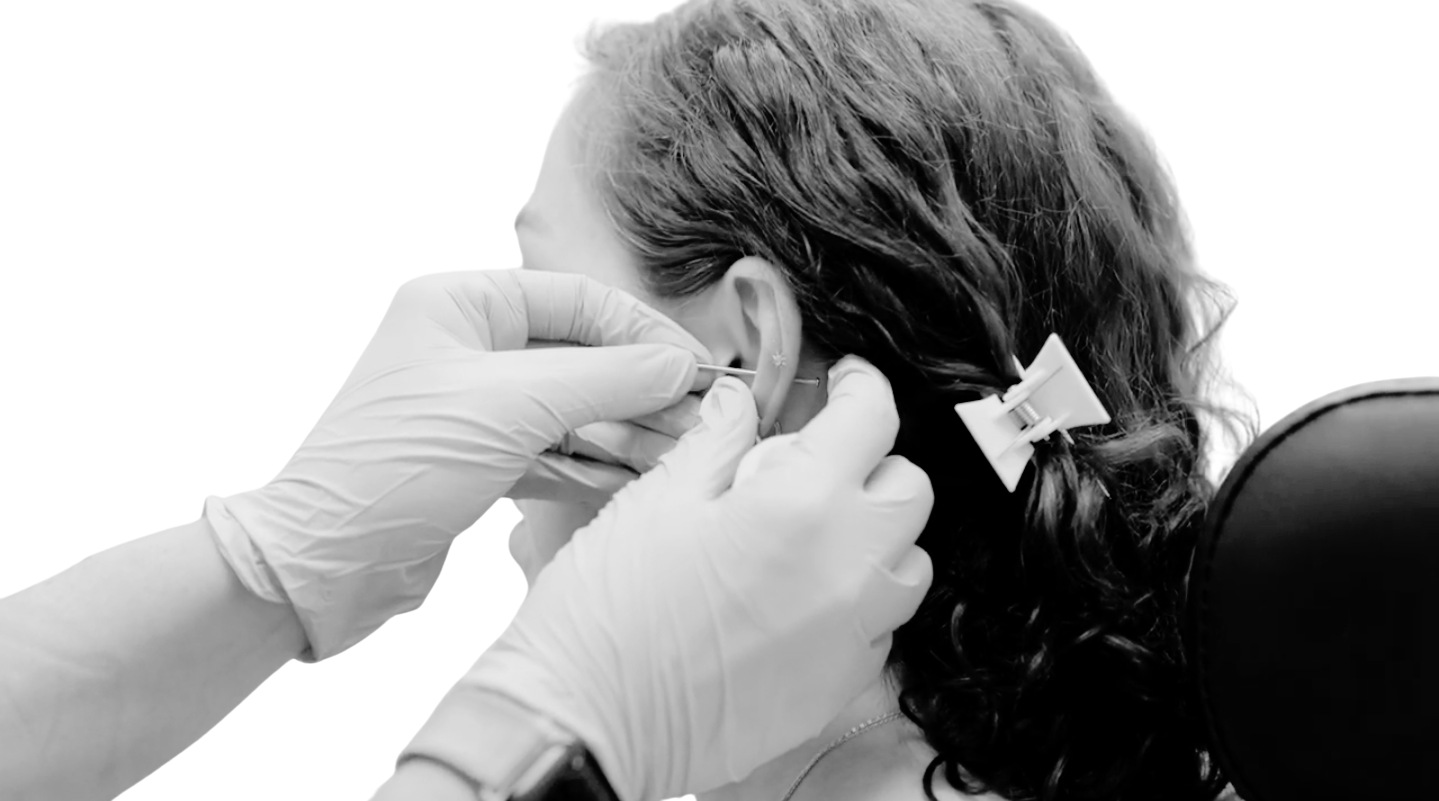 A person wearing gloves carefully inserts a piercing into another person's earlobe.