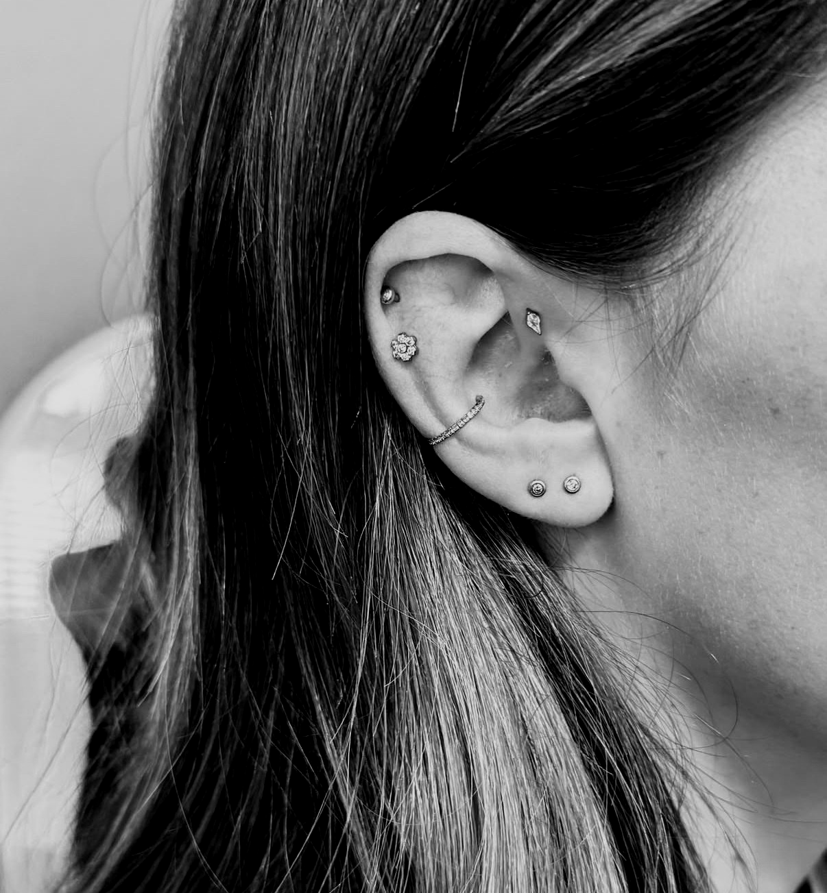 Black and white close-up of a right ear with five silver piercings along the cartilage and lobe.