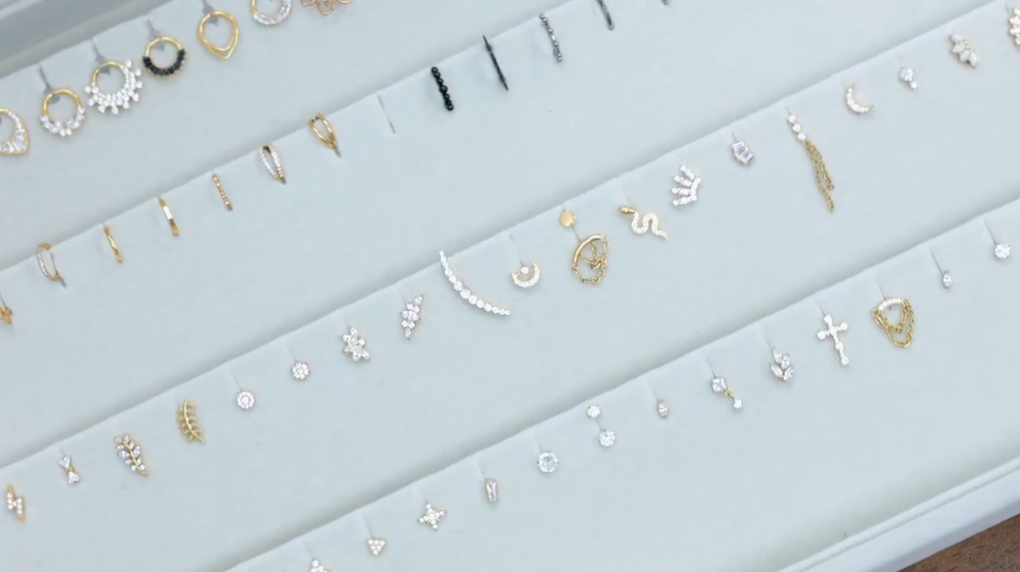 A jewelry display tray holding rows of various gold and silver stud earrings, hoops, and delicate charms.