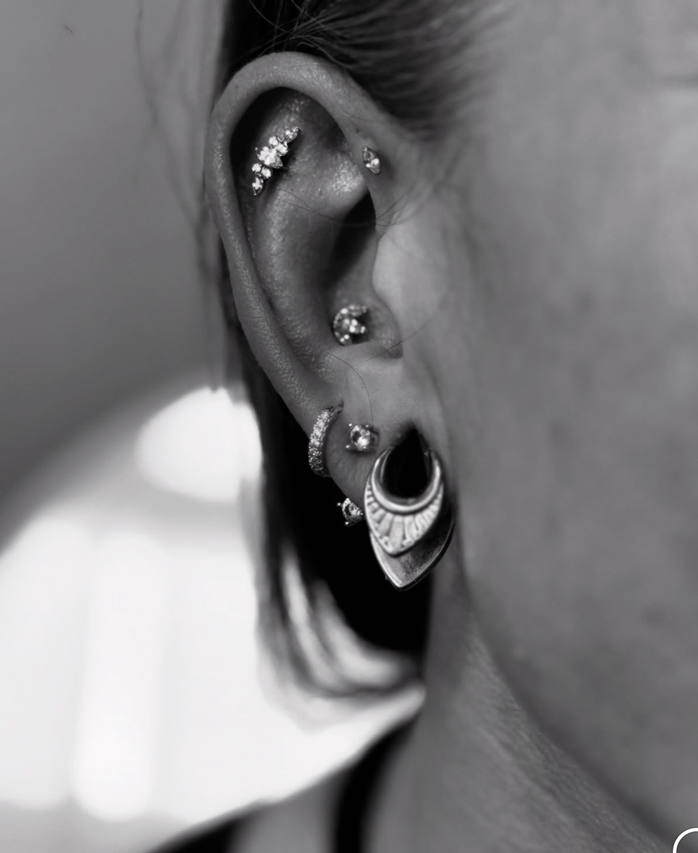 A close-up view of an ear featuring multiple silver piercings, including studs, a hoop, and decorative drop lobe jewelry.