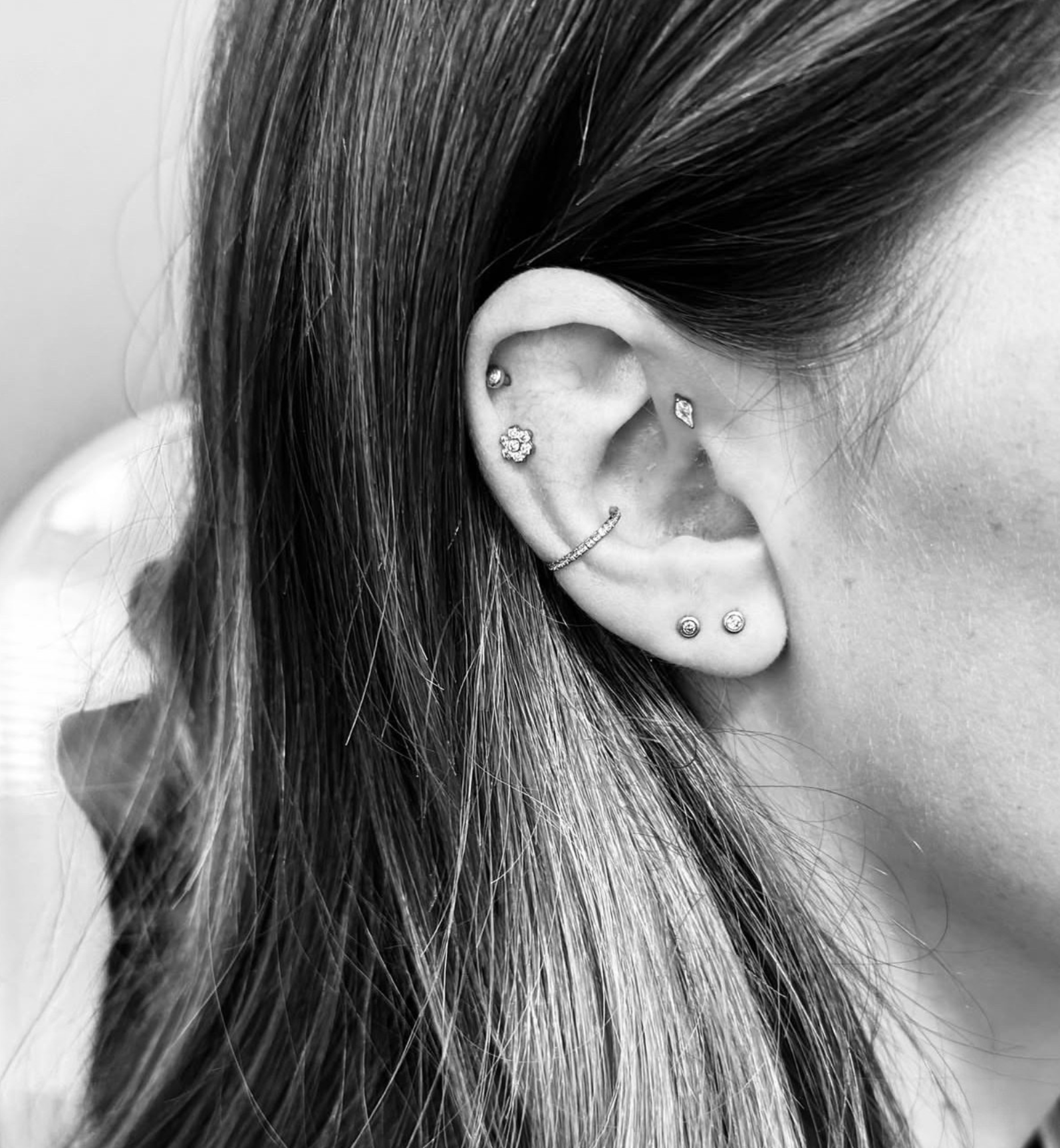 A close-up profile view of an ear featuring five silver-toned piercings, including studs, a crystal gem, and a hoop.