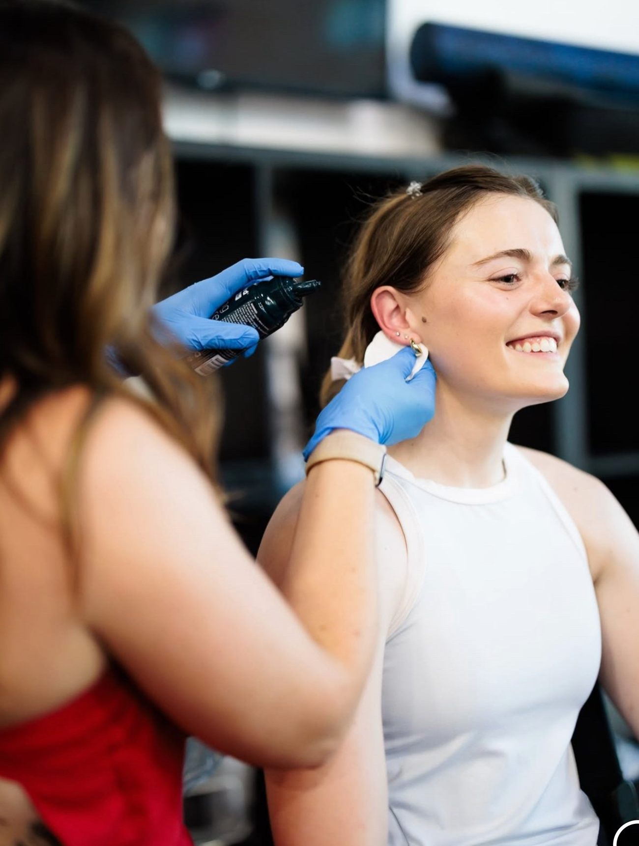 A person in blue gloves cleans a client's ear lobe with a cotton pad and spray in a studio setting.