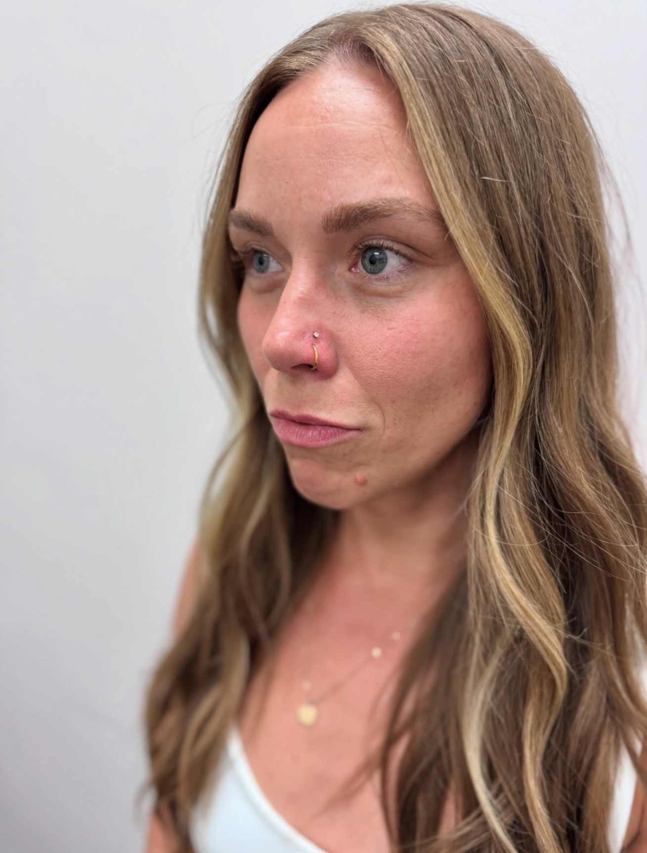 A person with long, blonde-highlighted brown hair wearing a small stud nose piercing, viewed from a slight angle.