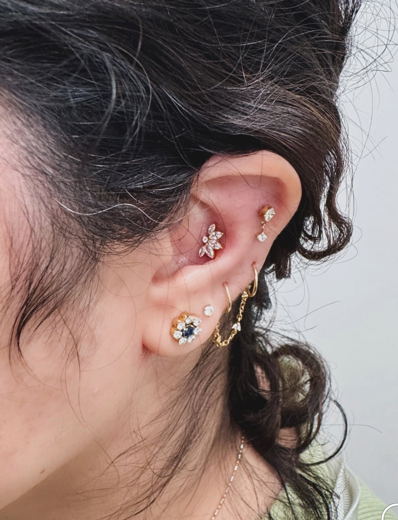 A side profile close-up of an ear decorated with five varied gold and gemstone earrings in multiple piercing locations.