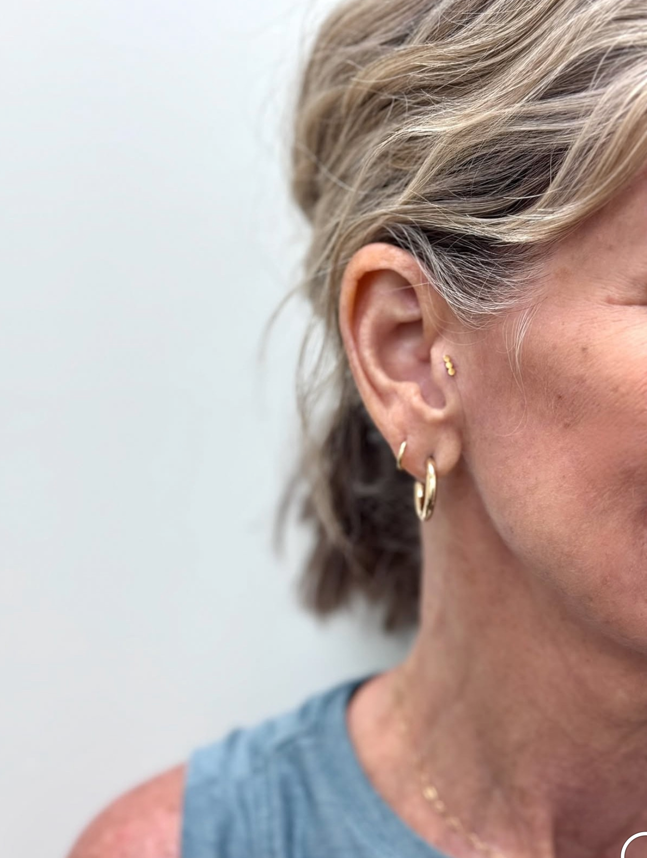 A person’s ear with a small gold tragus stud and two gold hoop earrings of different sizes.