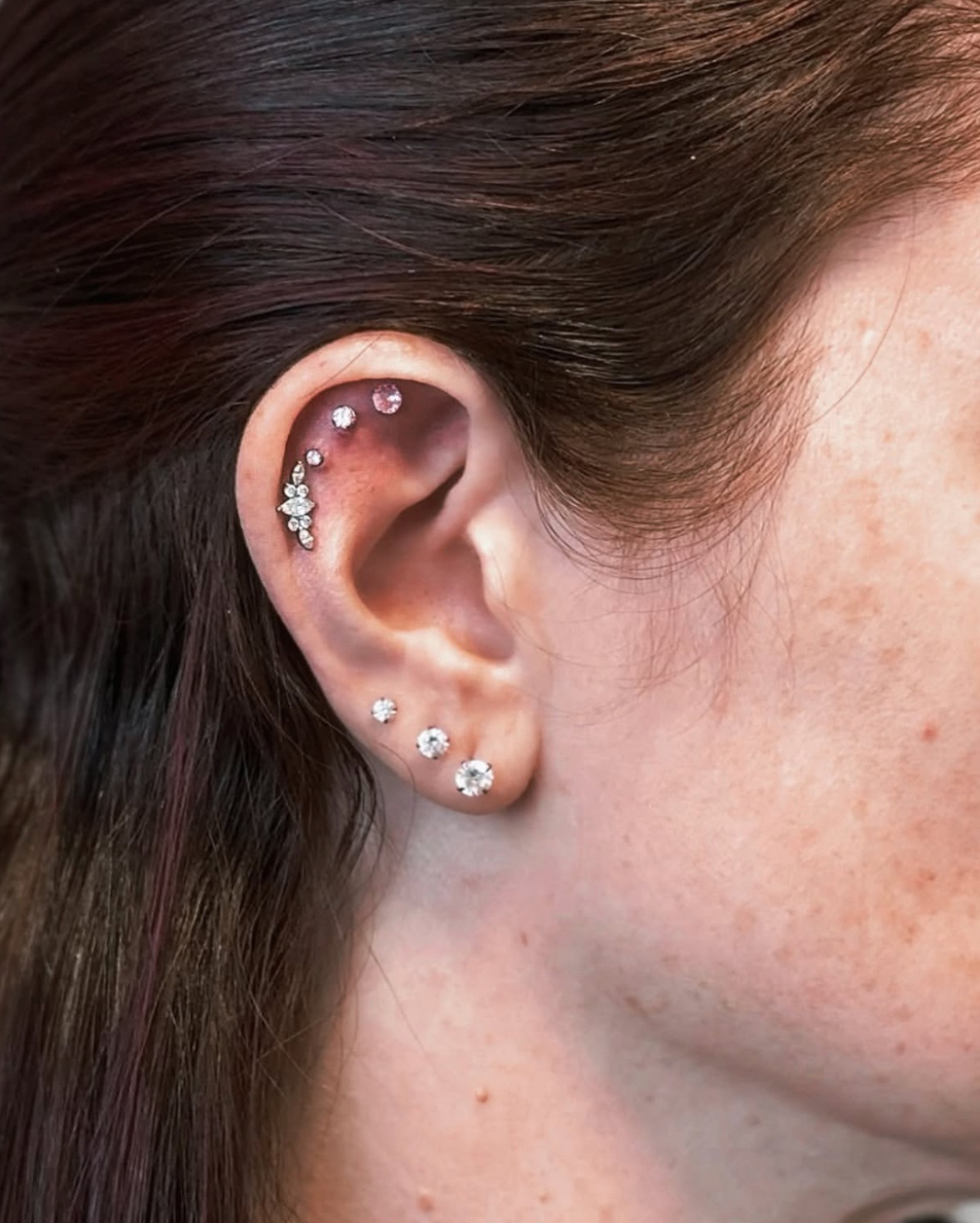 A profile view of an ear featuring three stud lobe piercings and three upper cartilage piercings with decorative studs.