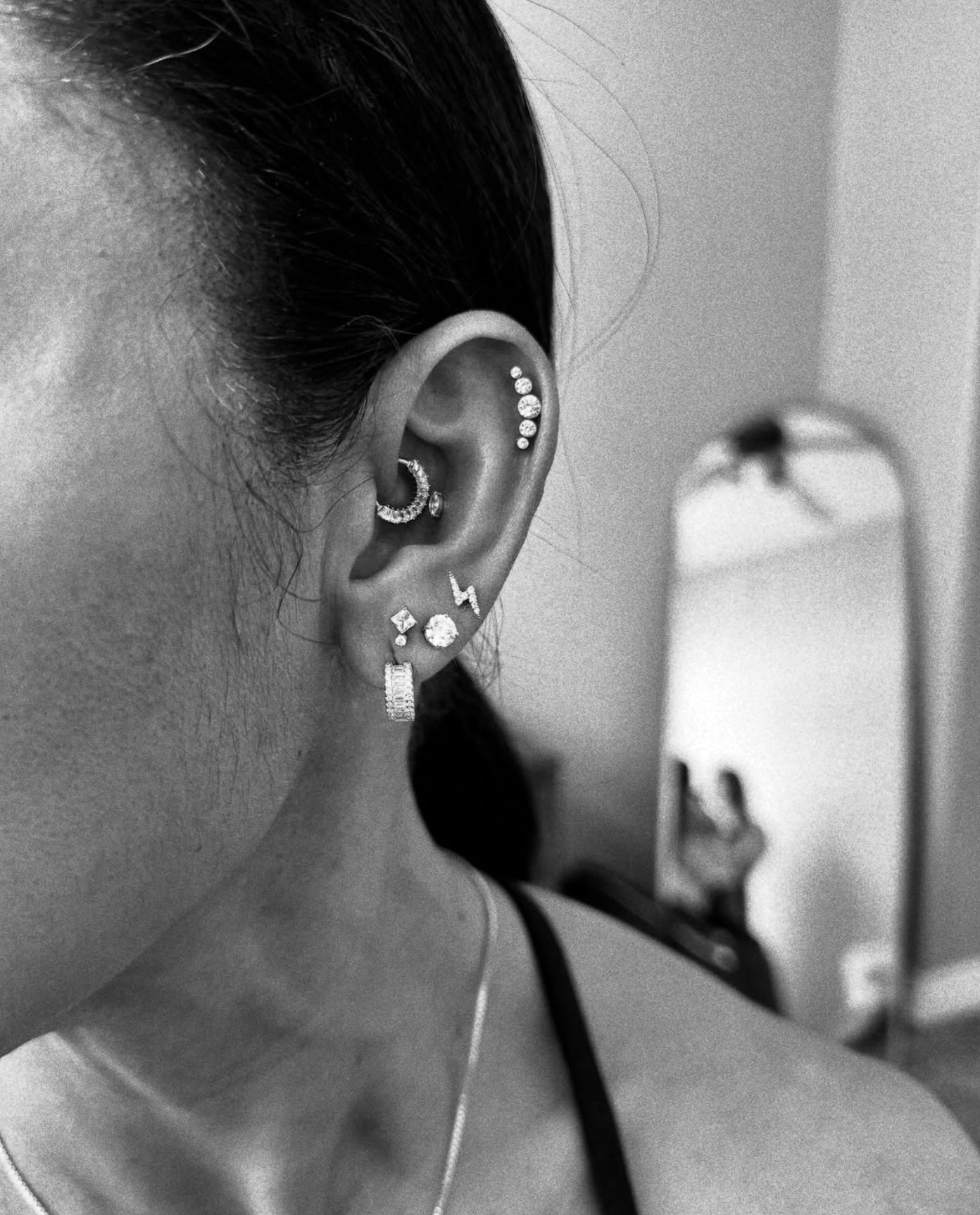 A side profile of an ear with multiple piercings, including a daith hoop, a flat stud, a lightning bolt, and hoop earrings.