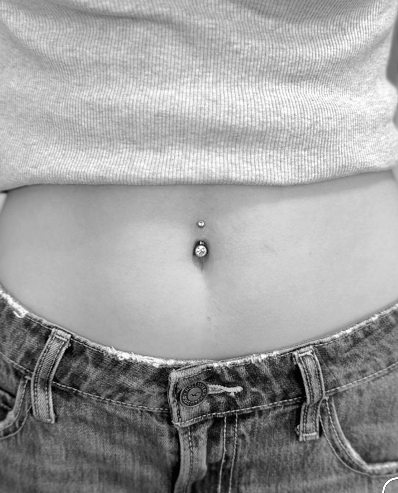 A midsection view of a person wearing a belly button piercing and a cropped top with jeans.