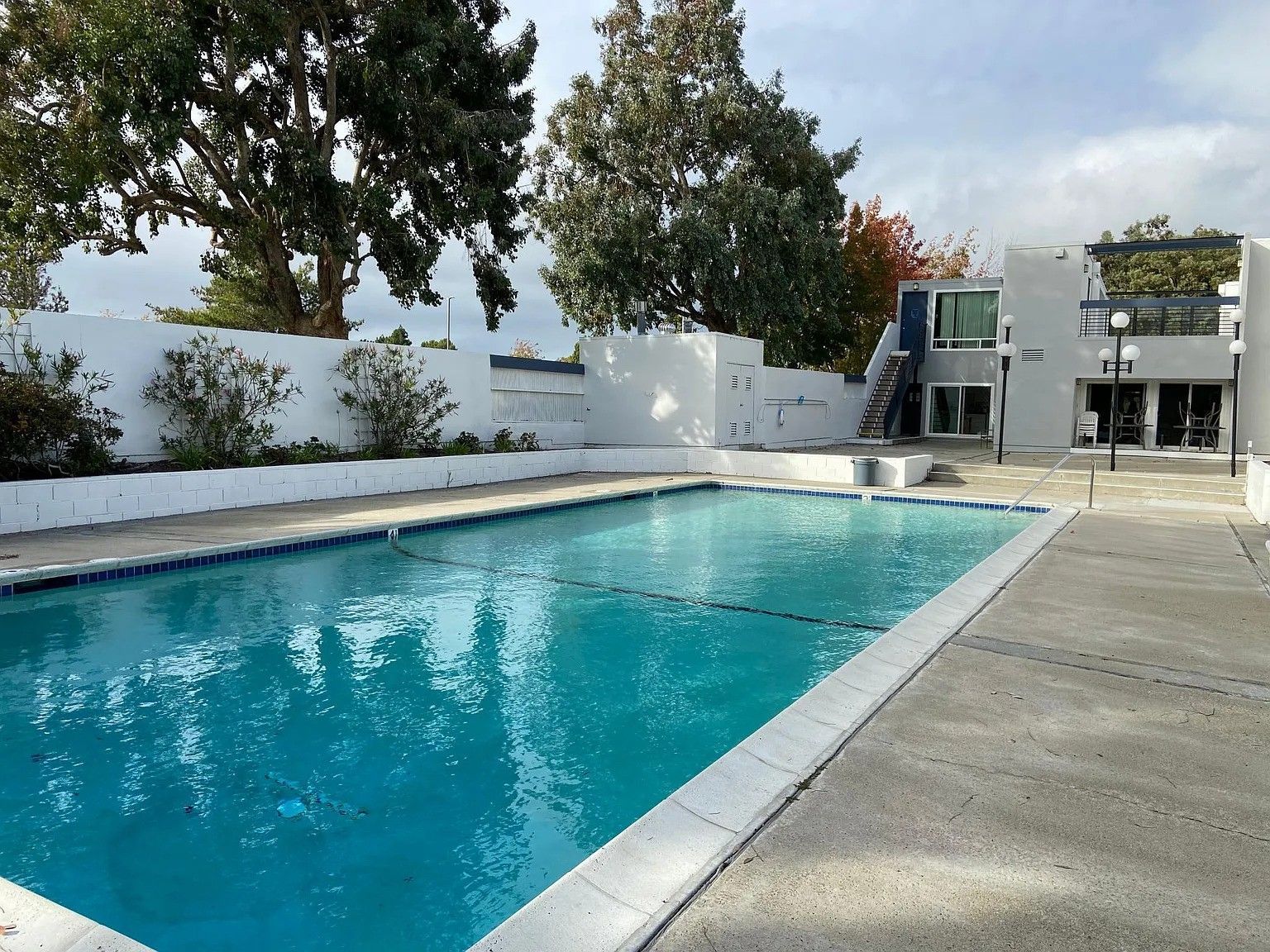 Outdoor pool with turquoise water beside a white patio and building in bright sunlight