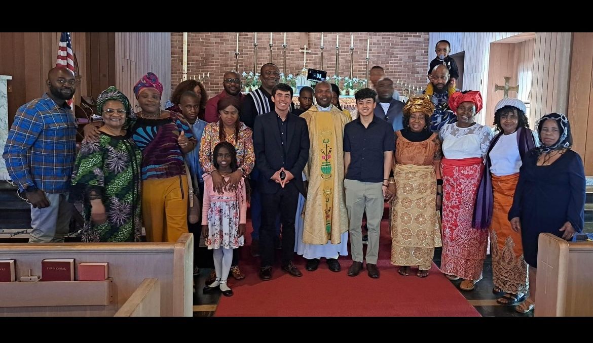 Group of people posing together indoors on a red-carpeted stage in front of brick walls.