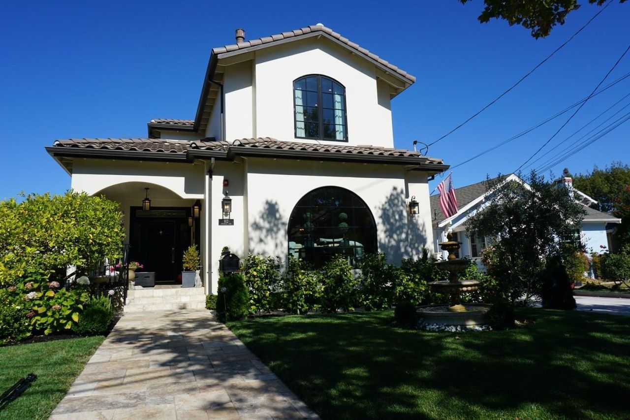 Front view of a stucco house with arched entry, blue shutters, and a landscaped front yard