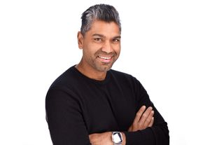 Man with shaved head adjusting black jacket collar over a white shirt.