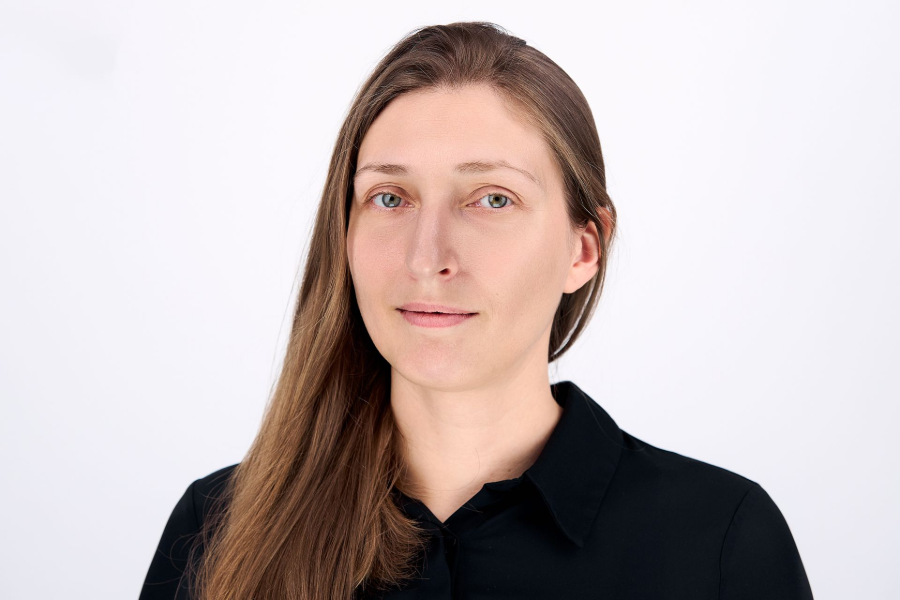 Woman with long brown hair, wearing a black shirt, looking at the camera. White background.