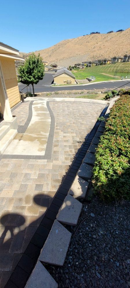 A brick walkway leading to a house with a hill in the background.