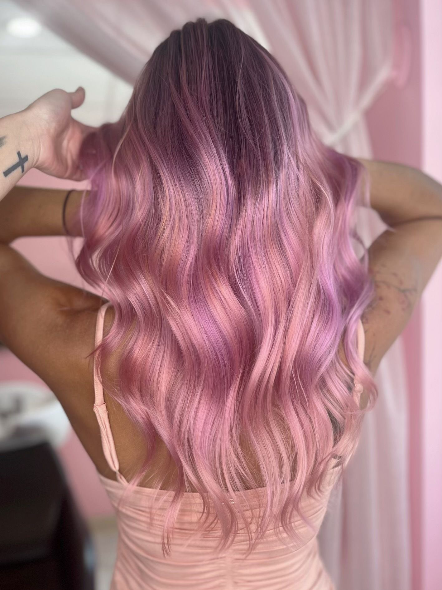 Long, wavy hair with a vibrant ombre color transition from deep purple roots to light pastel pink ends.