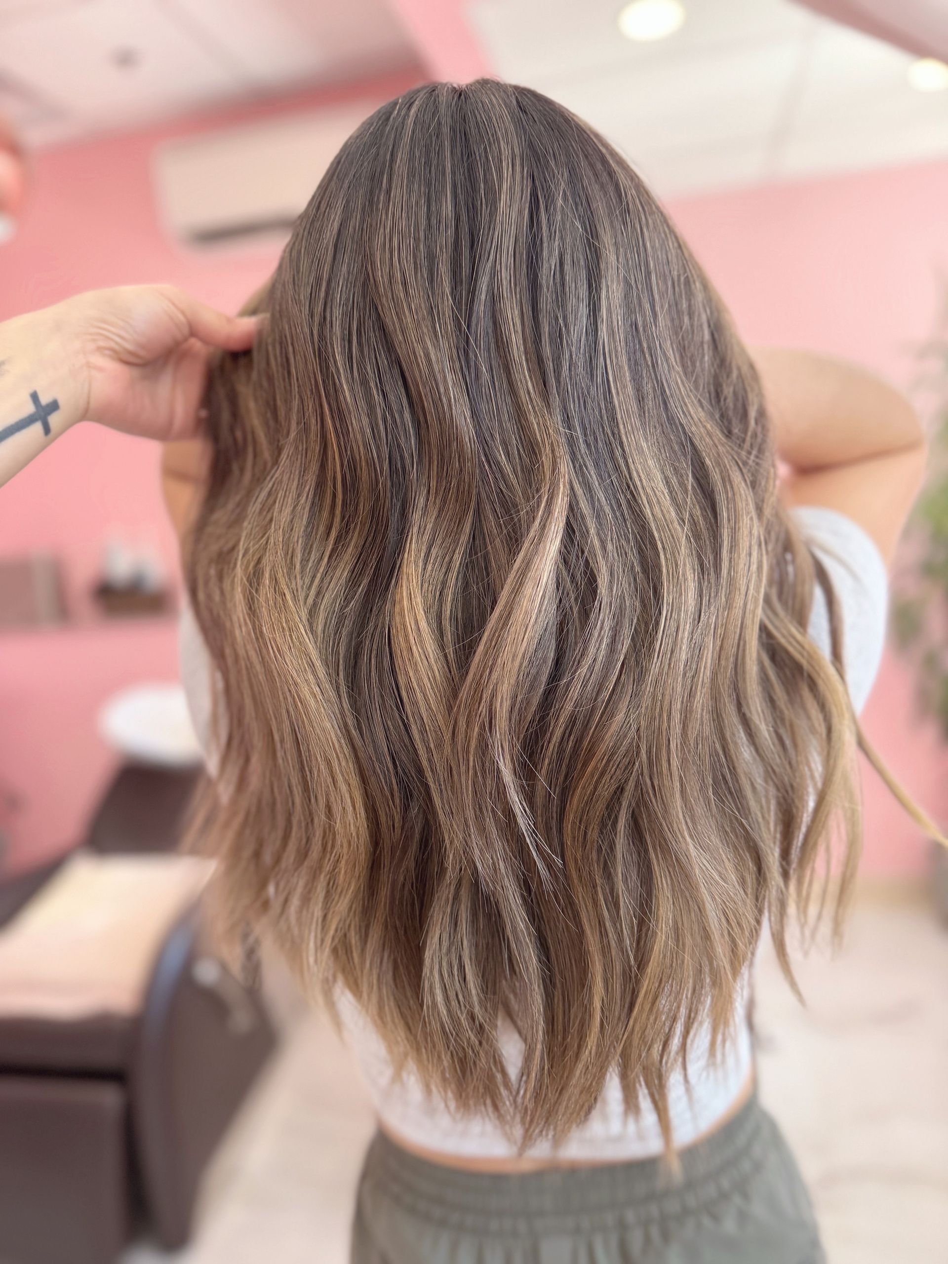 A person with long, wavy brown hair with blonde highlights styled in a salon, viewed from behind.