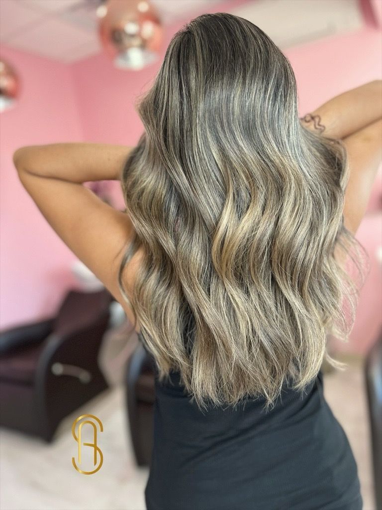 Back view of long, wavy, highlighted blonde hair in a salon with pink walls.