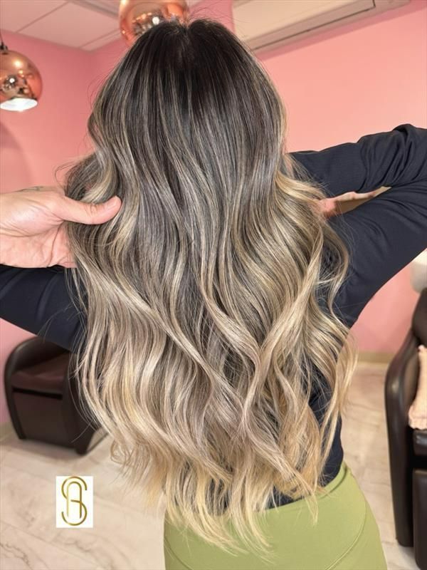 Long, wavy, multi-tonal hair with a dark root transition to light ash blonde ends in a salon setting.