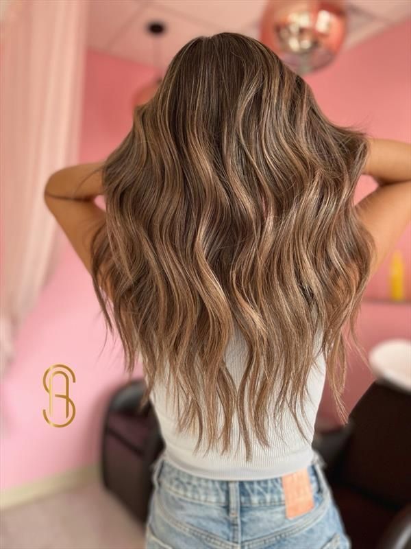 A view from behind of long, wavy, highlighted brown hair in a bright pink salon setting.