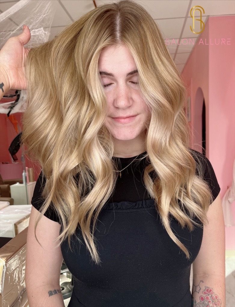 A person with long, voluminous, golden-blonde hair featuring a crimped texture and loose waves.