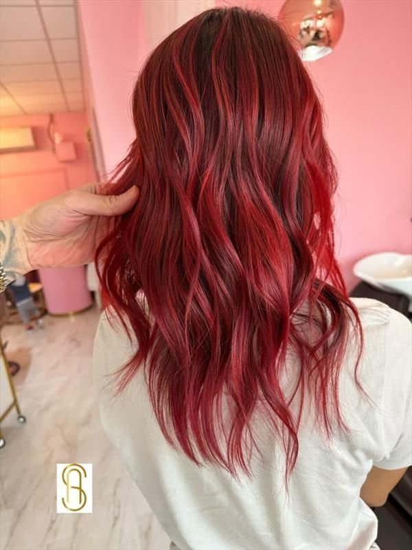A person with wavy, vibrant cherry-red hair styled in a salon, viewed from behind.