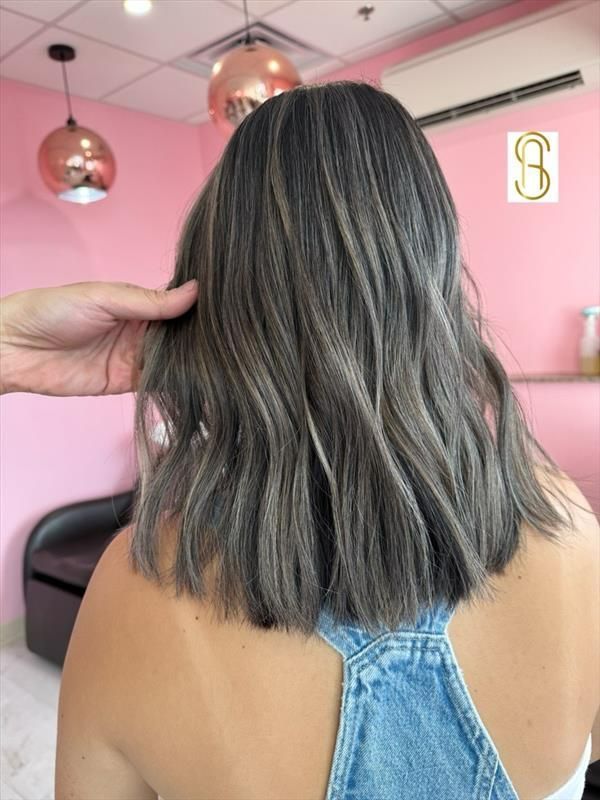 A shoulder-length, wavy hairstyle featuring ash-grey tones and dark highlights, viewed from behind in a salon setting.