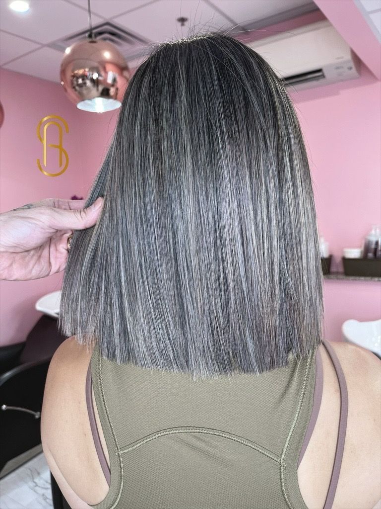 A person with a grey, chin-length textured bob cut in a salon, held by a stylist's hand against a pink background.