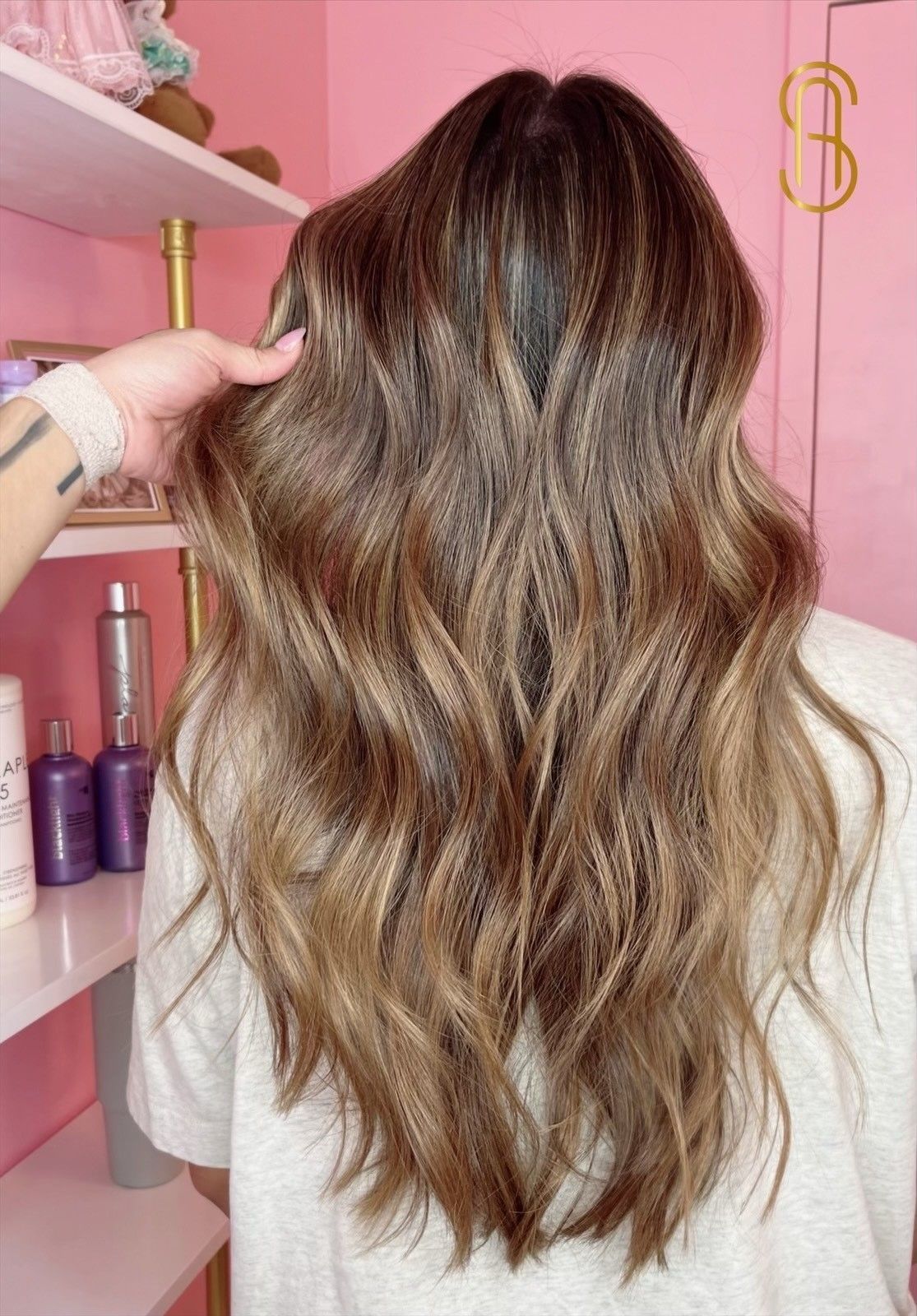 Long, wavy, brunette hair with golden-brown highlights styled in a salon, viewed from behind.