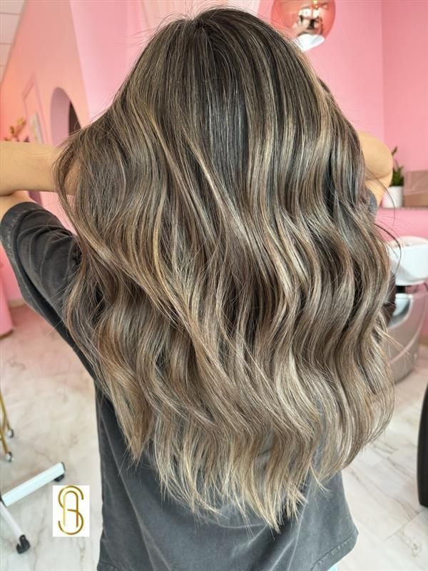 Back view of long, wavy hair with dimensional ash-brown highlights and balayage in a salon setting.