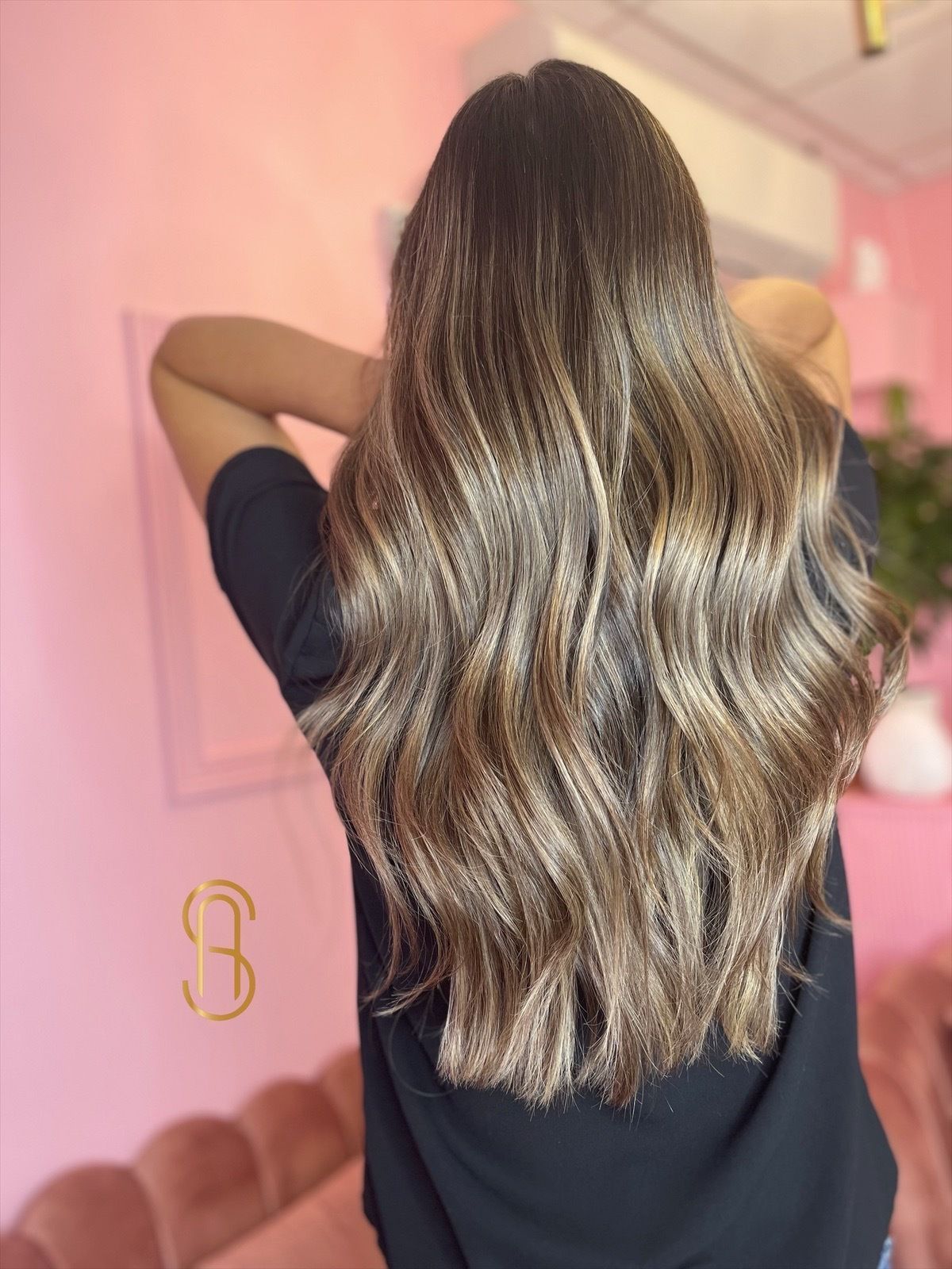 Back view of long, wavy, highlighted brown hair in a bright pink room.