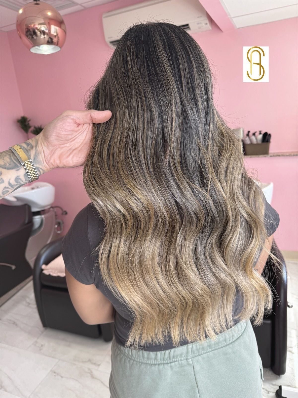 A person shows off their long, wavy brown hair with a blonde ombre fade, styled in a professional hair salon.