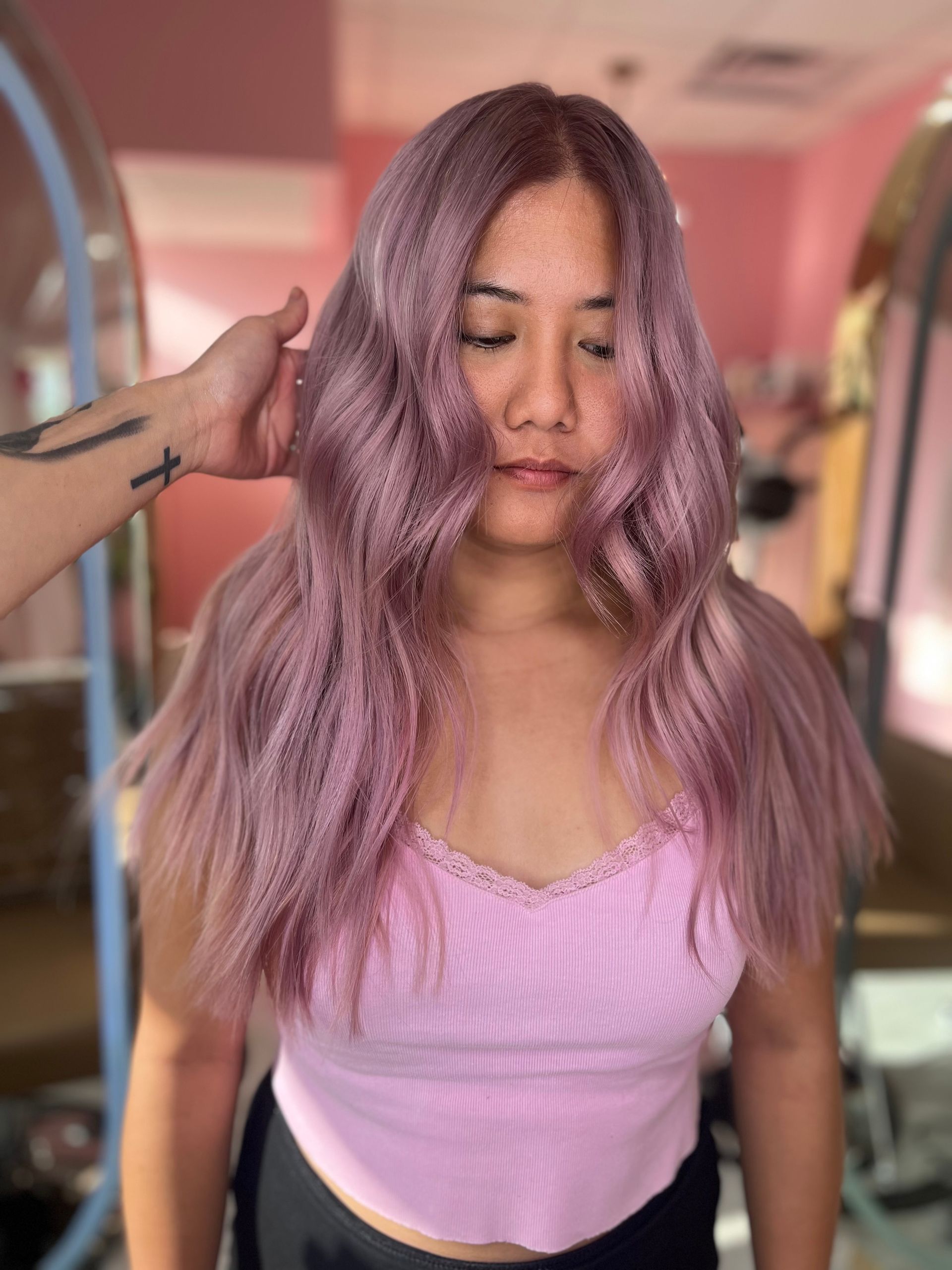 A stylist combs wavy, highlighted hair in a salon while the client sits in a chair.