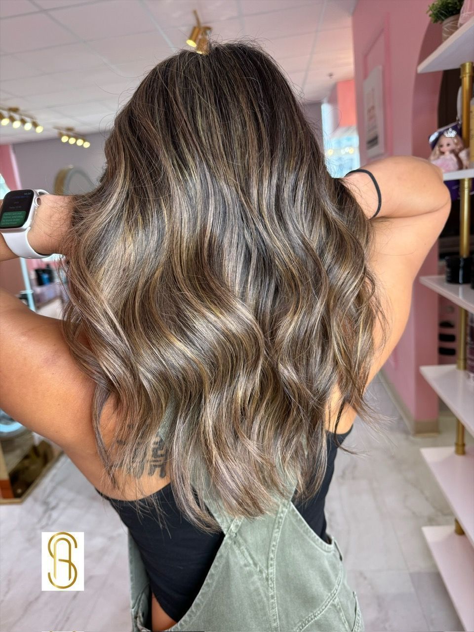 Person with medium-length, wavy, highlighted brunette hair viewed from behind in a salon setting.