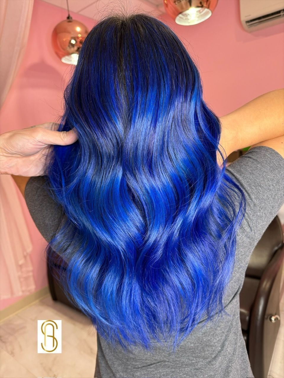 Person with long, wavy hair dyed in vibrant shades of blue and deep indigo, viewed from the back.