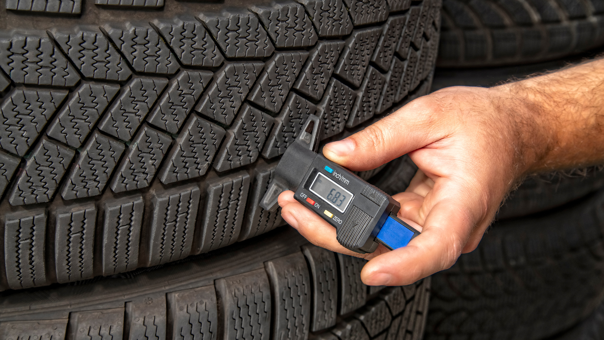 Hand checking tire tread depth with a gauge on a car tire.