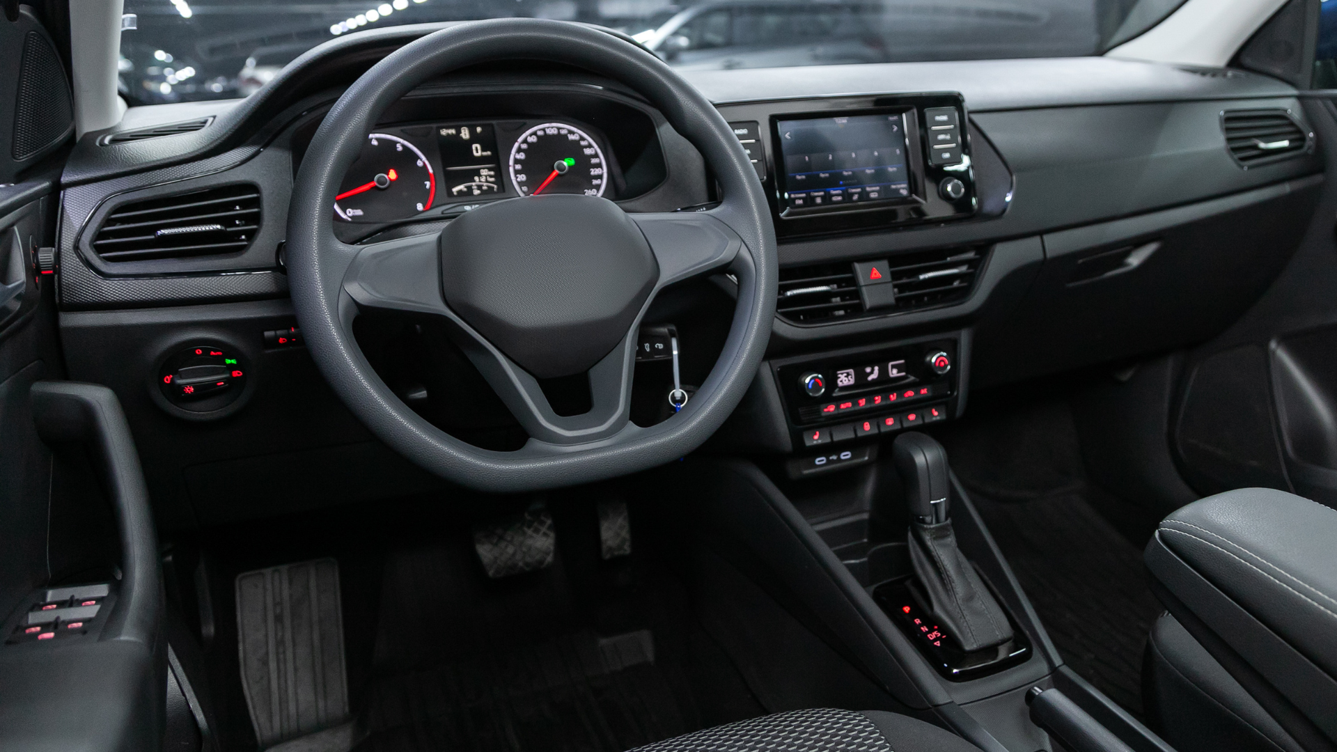 Modern car interior with steering wheel, dashboard display, and center console in black and red accents