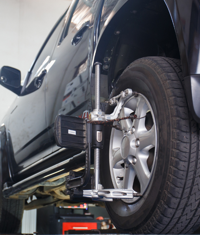 Black car undergoing wheel alignment in a garage.