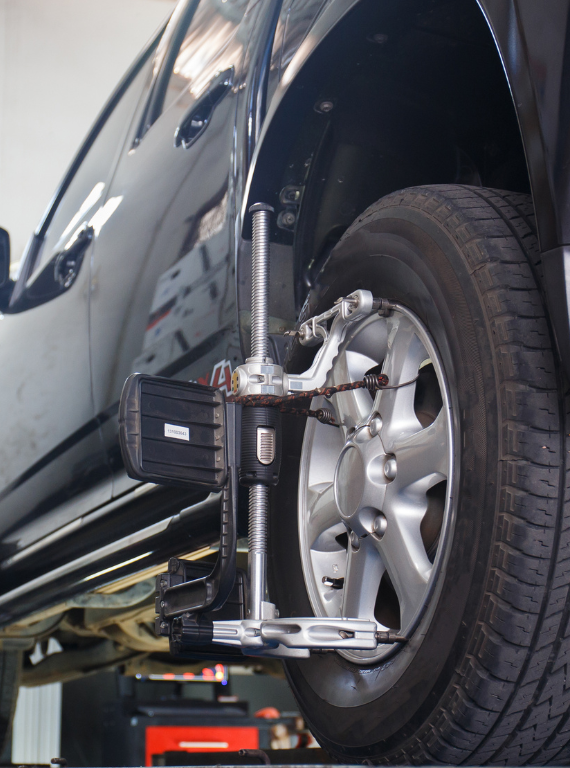 Black car undergoing wheel alignment in a garage.