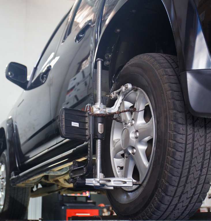 Black car undergoing wheel alignment in a garage.