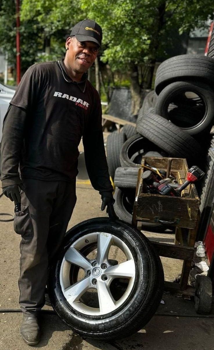 A man is standing next to a tire in front of a pile of tires.