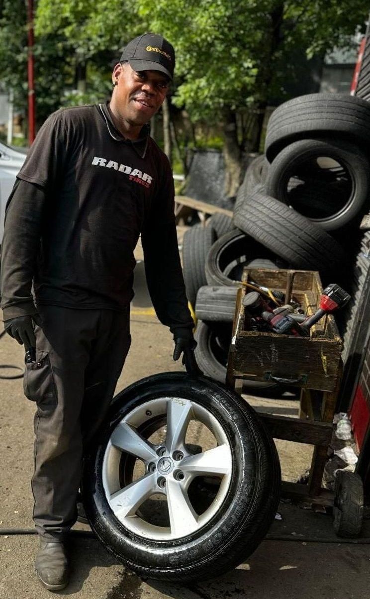 A man is standing next to a tire in front of a pile of tires.