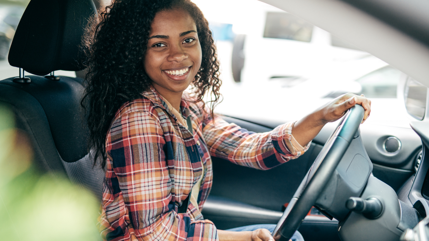 Smiling driver in plaid shirt sitting behind the wheel of a car