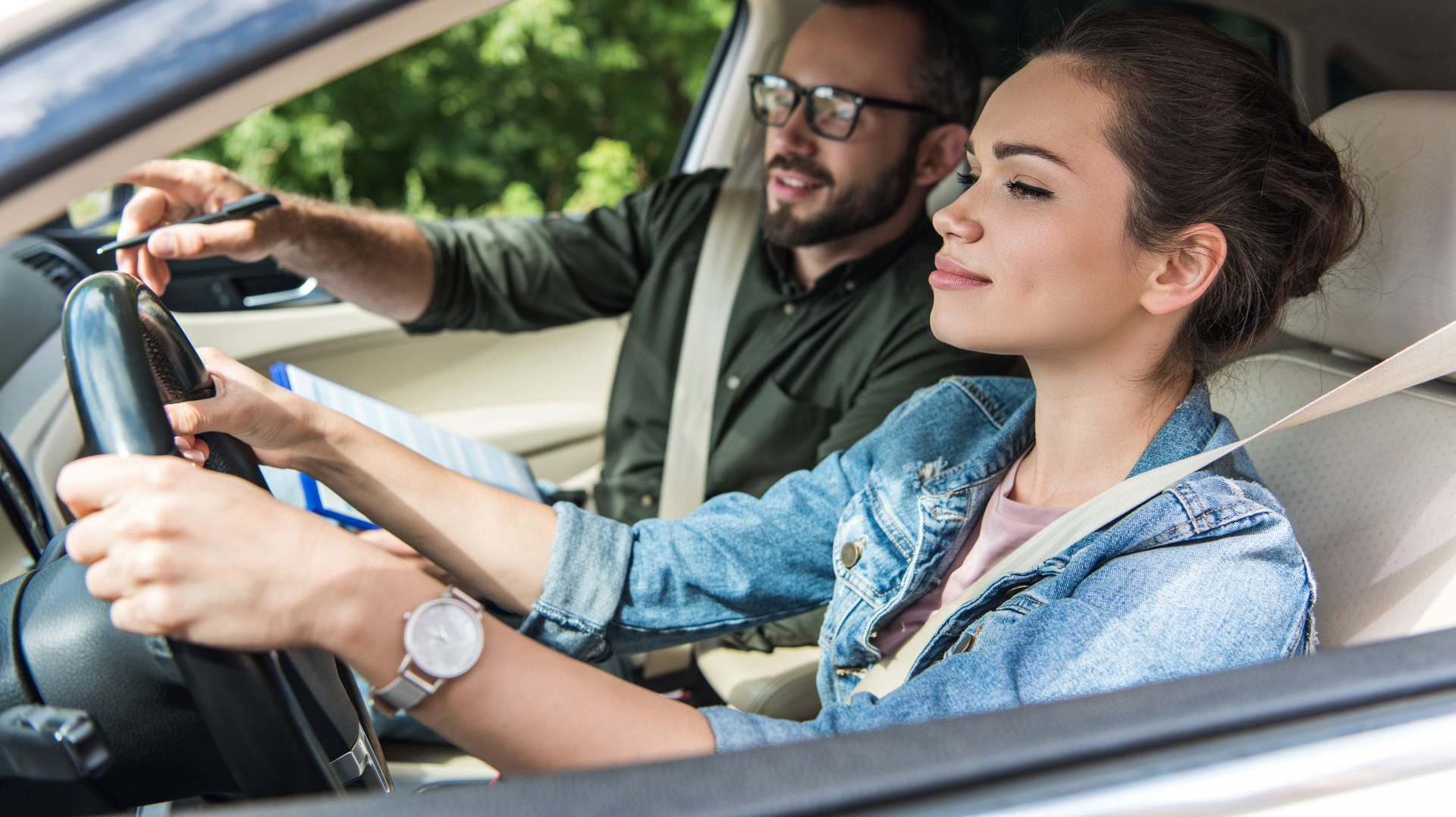 Two people sitting in a car, the driver focused ahead while the passenger appears to be learning to drive.